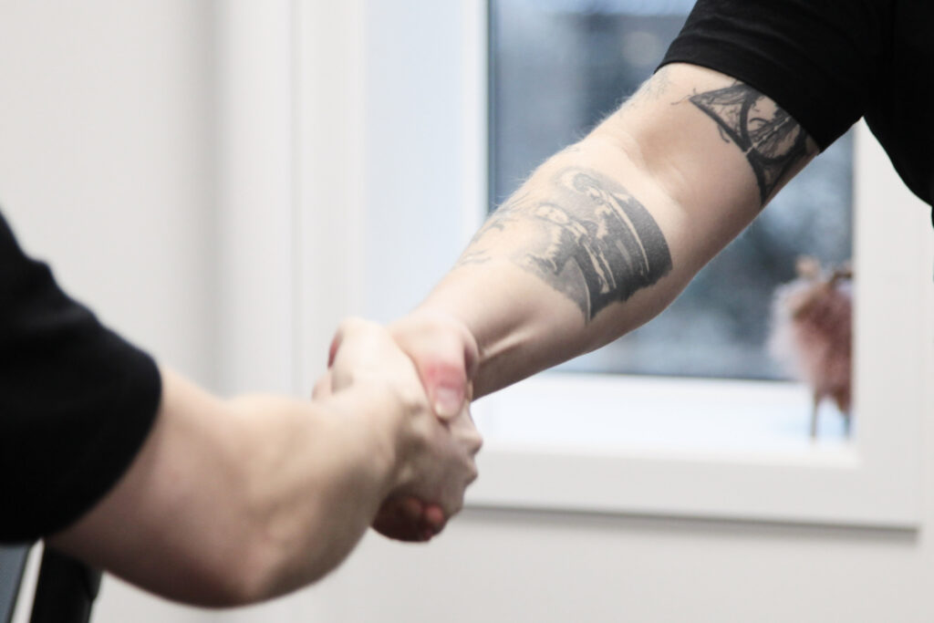 To personer håndhilser foran en kontor- eller forretningsbakgrunn, som symboliserer avslutningen av en vellykket domenesalgsavtale.