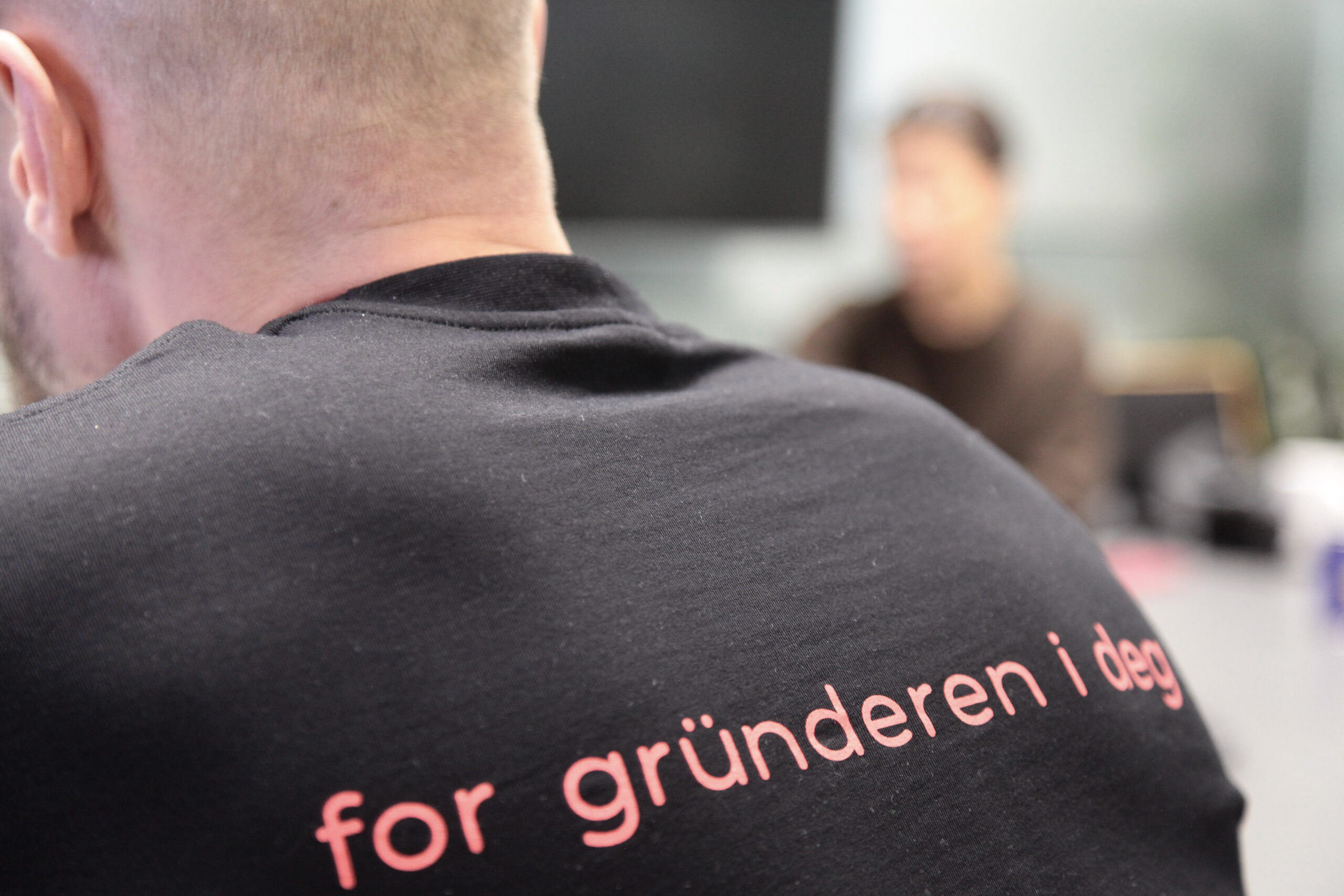 Uniweb-ansatt med teksten 'for gründeren i deg' på skjorten, sett bakfra i et kontormiljø