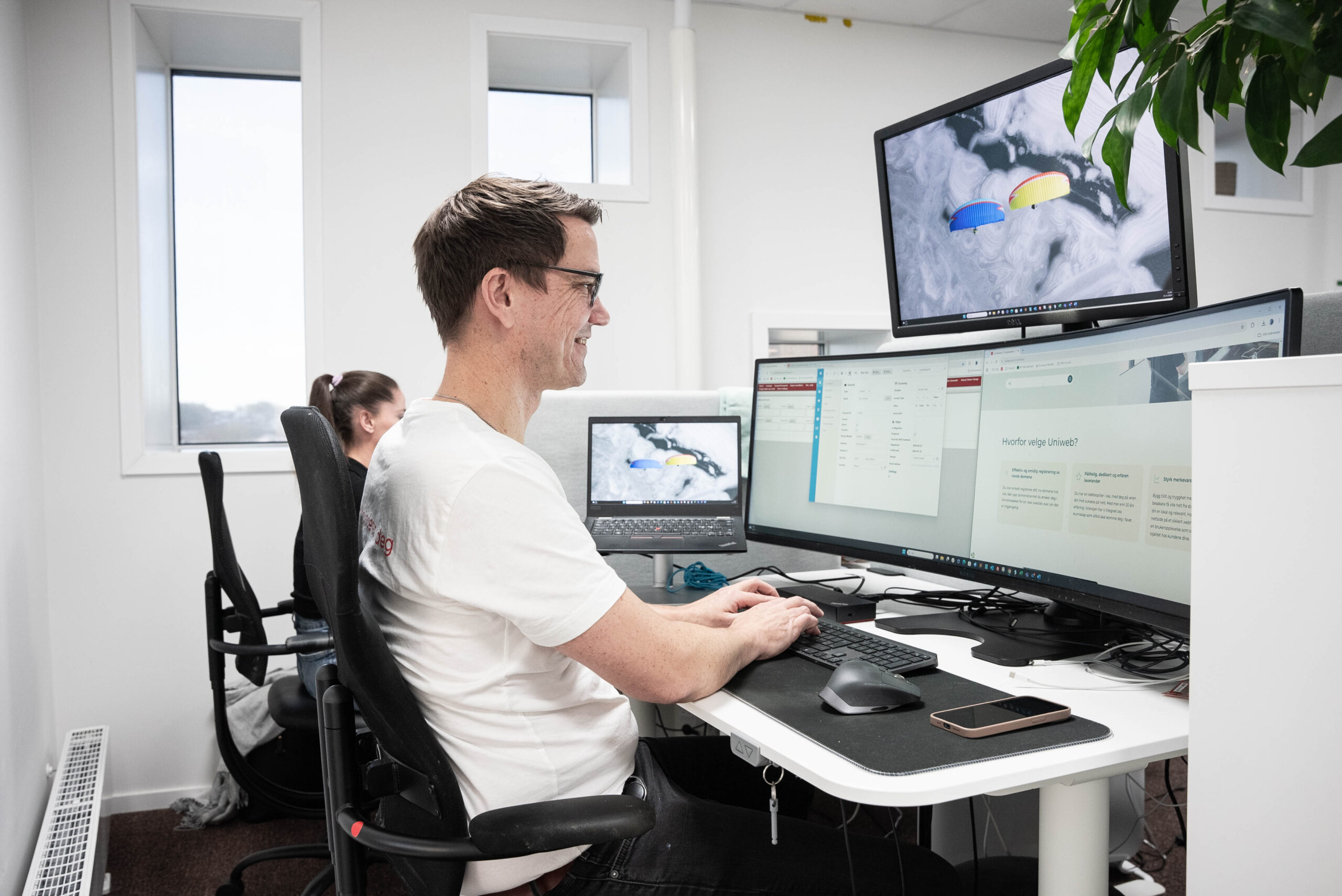 IT-spesialist sitter ved pult med flere skjermer som viser serverstatus og kontrollpanel for webhotell-administrasjon.